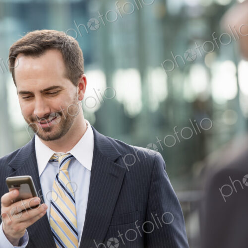City life. People on the move. A man in a business suit checking his messages on his… City life. People on the move. A man in a business suit checking his messages on his…