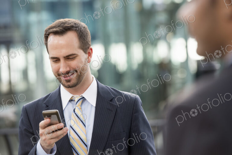 City life. People on the move. A man in a business suit checking his messages on his…