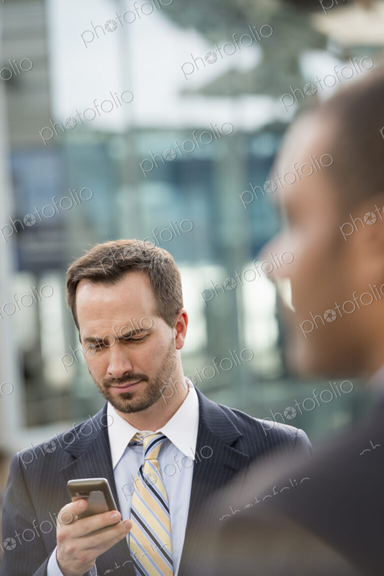 City life. People on the move. A man in a business suit checking his messages on his…