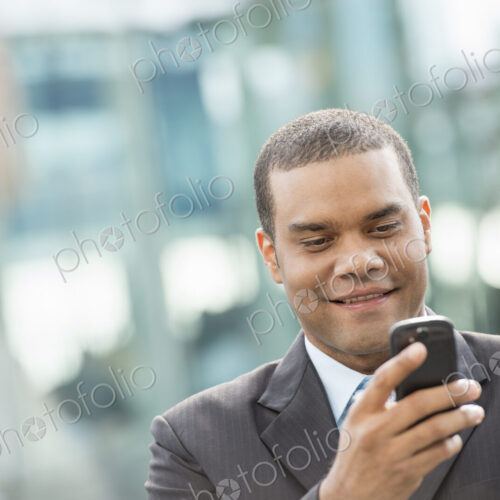 City life. People on the move. A man in a business suit checking his messages on his… City life. People on the move. A man in a business suit checking his messages on his…