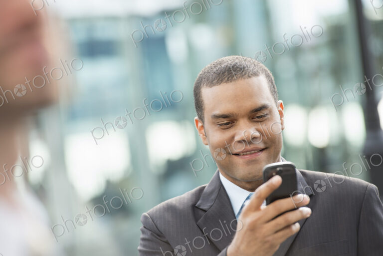 City life. People on the move. A man in a business suit checking his messages on his…