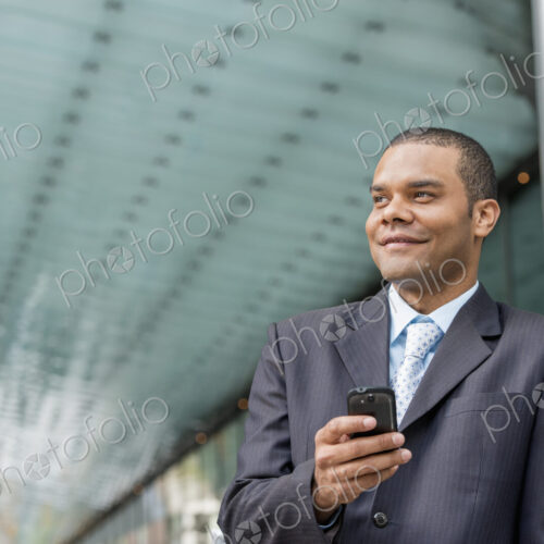 City life. People on the move. A man in a business suit checking his messages on his… City life. People on the move. A man in a business suit checking his messages on his…