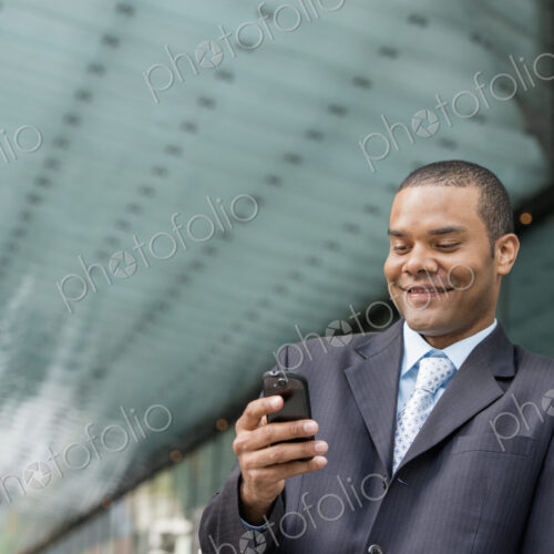 City life. People on the move. A man in a business suit checking his messages on his… City life. People on the move. A man in a business suit checking his messages on his…