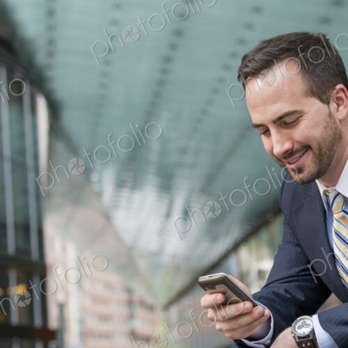 City life. People on the move. A man in a business suit checking his messages on his… City life. People on the move. A man in a business suit checking his messages on his…