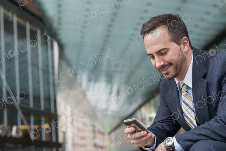 City life. People on the move. A man in a business suit checking his messages on his…