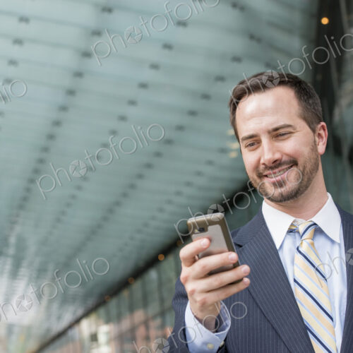 City life. People on the move. A man in a business suit checking his messages on his… City life. People on the move. A man in a business suit checking his messages on his…