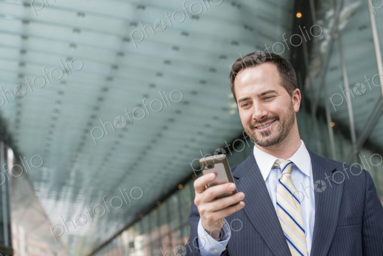 City life. People on the move. A man in a business suit checking his messages on his…
