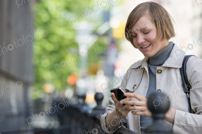 City life. People on the move. A woman in a jacket checking her smart phone.