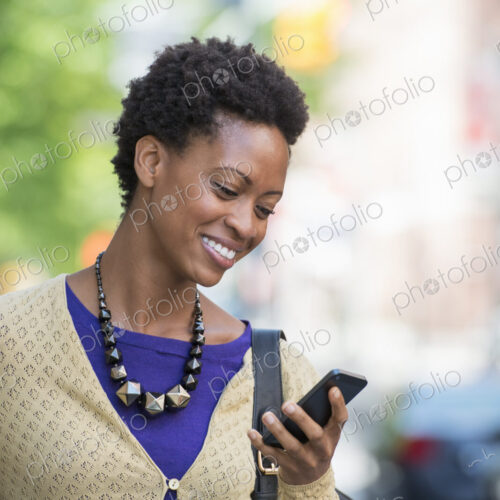 City life. People on the move. A woman in a purple dress checking her smart phone. City life. People on the move. A woman in a purple dress checking her smart phone.