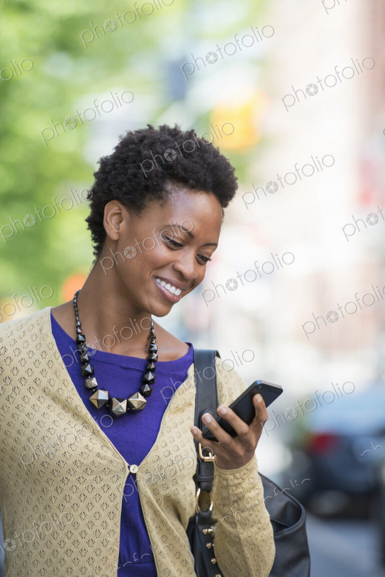 City life. People on the move. A woman in a purple dress checking her smart phone.