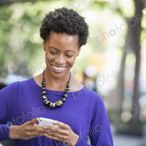 City life. People on the move. A woman in a purple dress checking her smart phone. City life. People on the move. A woman in a purple dress checking her smart phone.