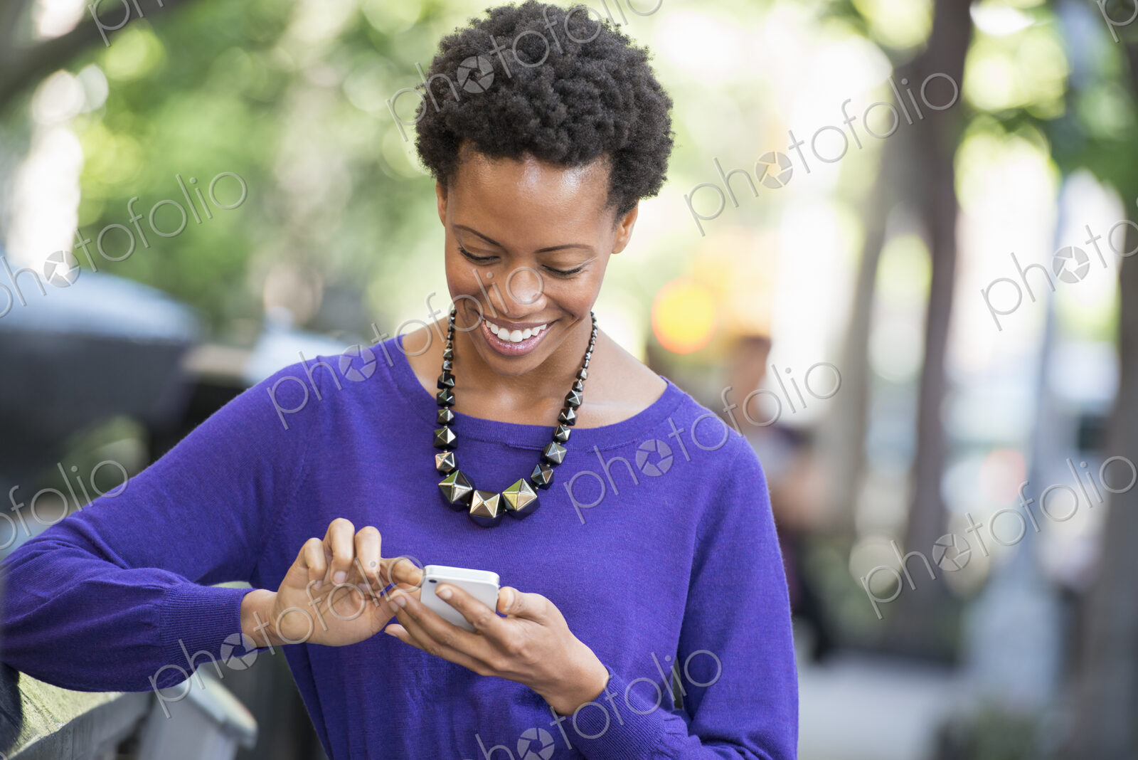 City life. People on the move. A woman in a purple dress checking her smart phone.