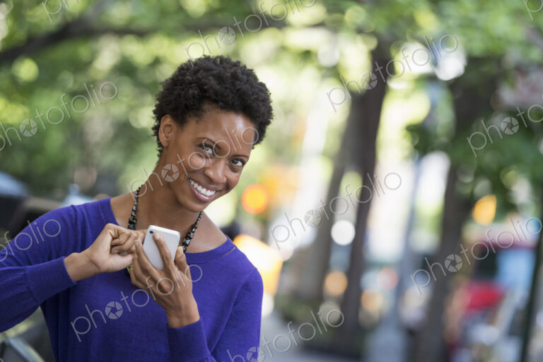 City life. People on the move. A woman in a purple dress checking her smart phone.