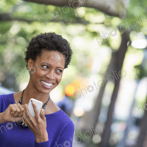 City life. People on the move. A woman in a purple dress checking her smart phone. City life. People on the move. A woman in a purple dress checking her smart phone.