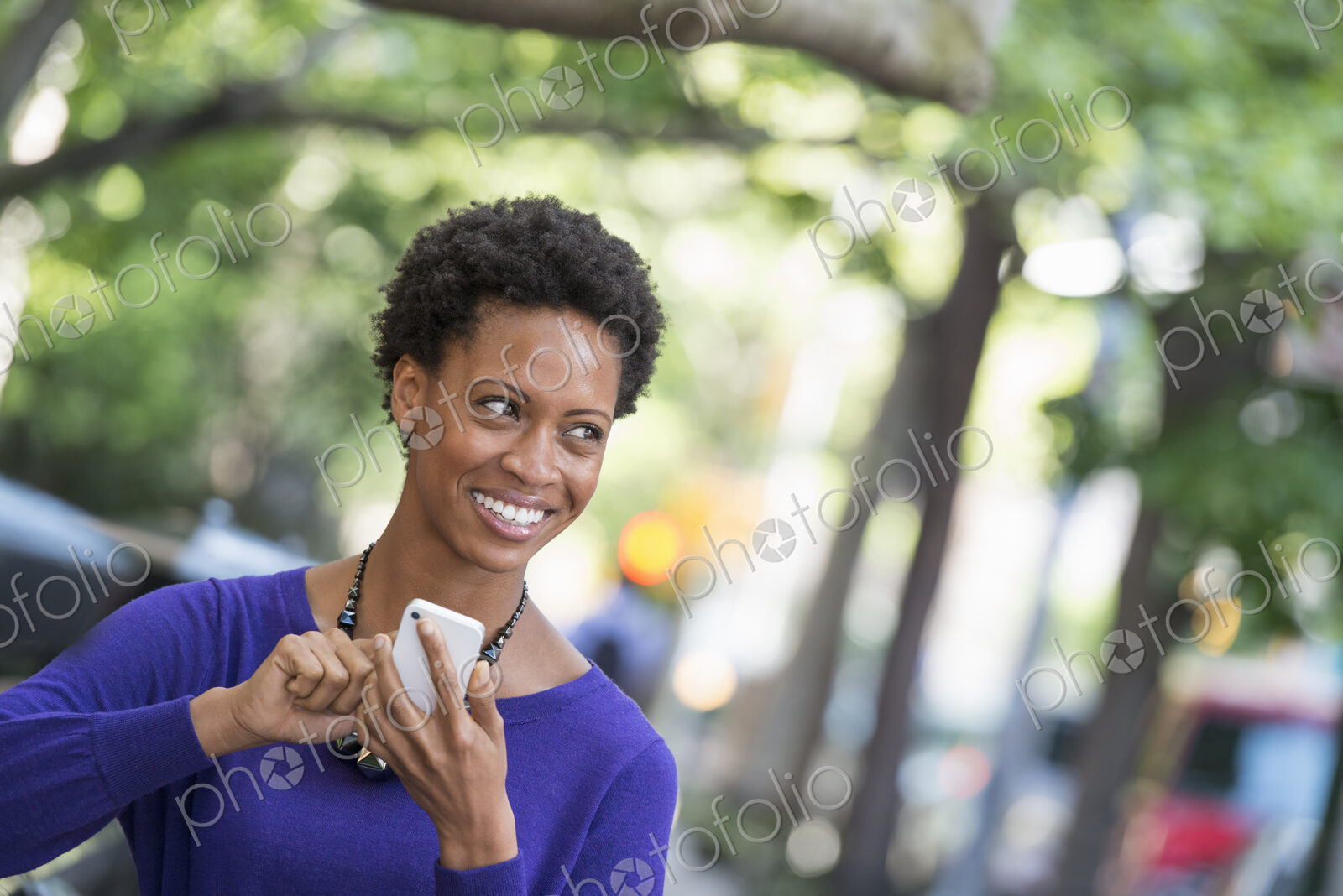 City life. People on the move. A woman in a purple dress checking her smart phone.