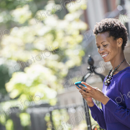 City life. People on the move. A woman in a purple dress checking her smart phone. City life. People on the move. A woman in a purple dress checking her smart phone.