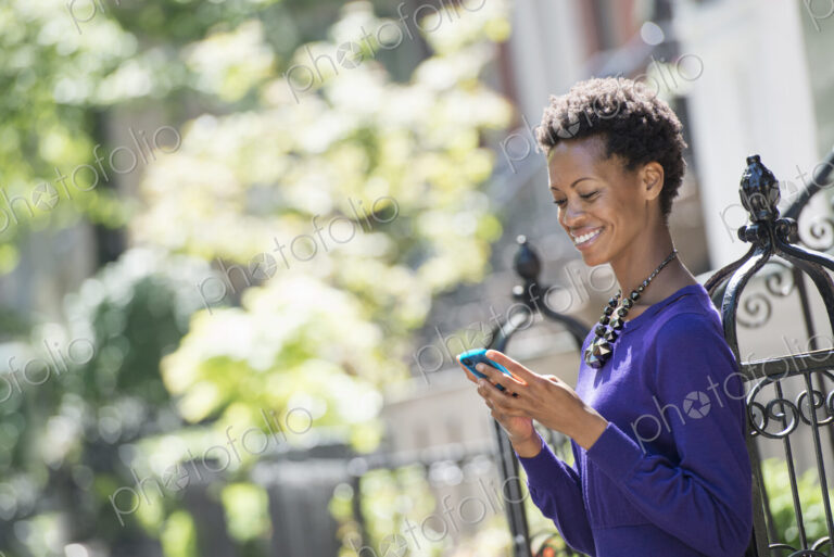 City life. People on the move. A woman in a purple dress checking her smart phone.