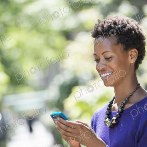 City life. People on the move. A woman in a purple dress checking her smart phone.