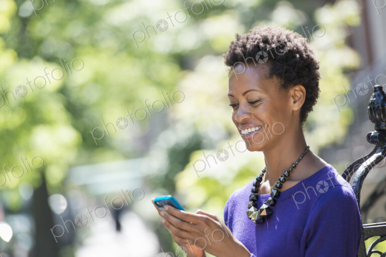 City life. People on the move. A woman in a purple dress checking her smart phone.