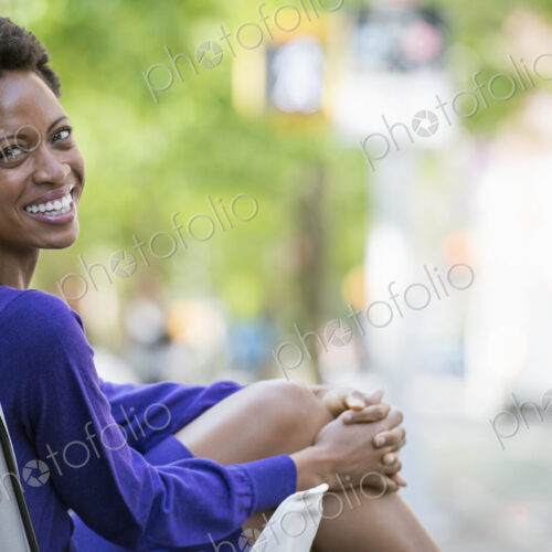 City life. People on the move. A woman in a purple dress, sitting in a canvas camping…