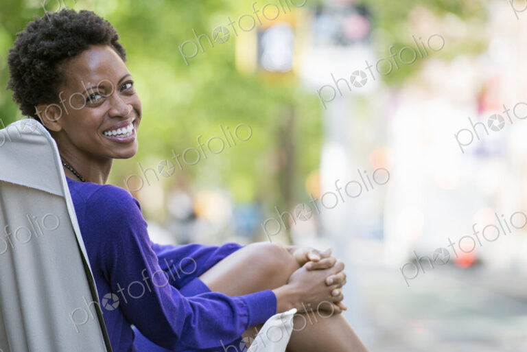 City life. People on the move. A woman in a purple dress, sitting in a canvas camping…