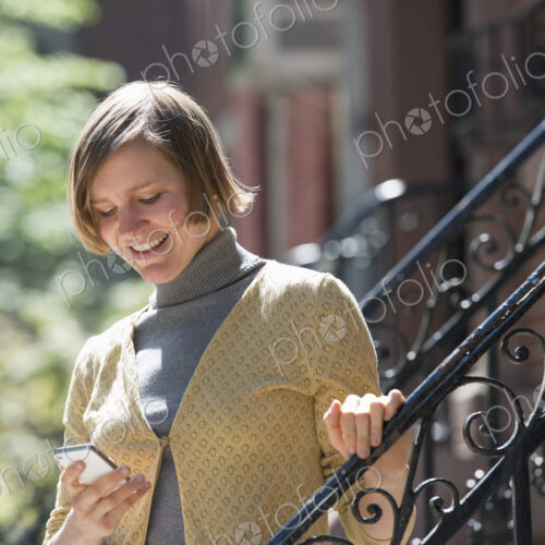 City life. People on the move. A woman on steps outside a townhouse, checking her…