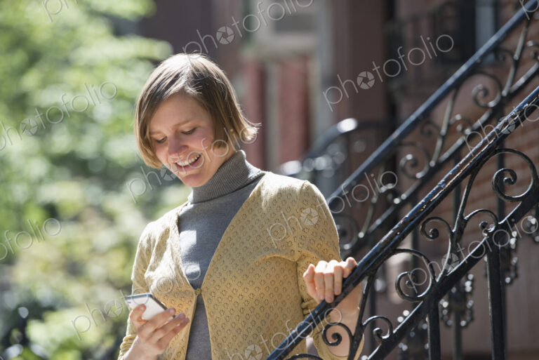 City life. People on the move. A woman on steps outside a townhouse, checking her…