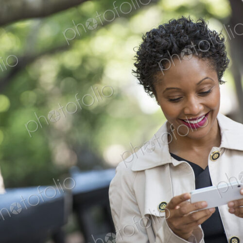 City life. People on the move. A woman outdoors in the park, checking her smart phone.
