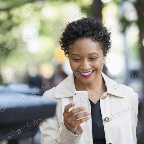 City life. People on the move. A woman outdoors in the park, checking her smart phone.