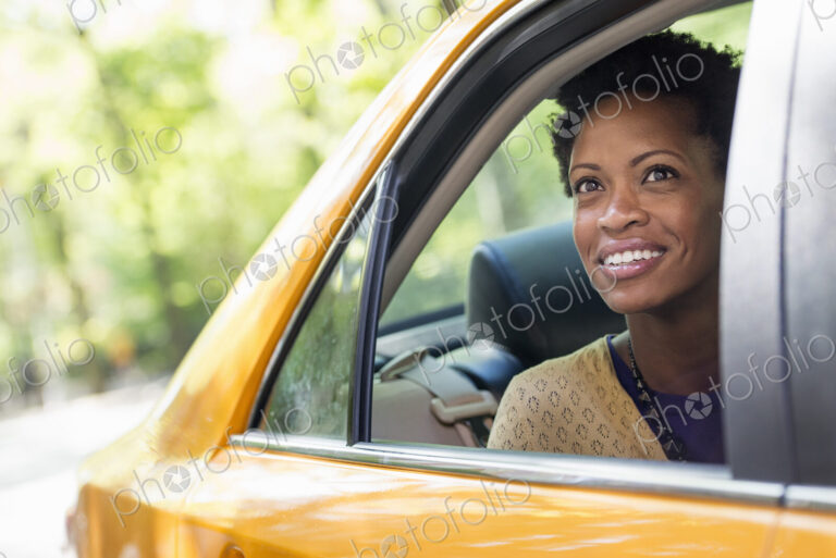 City life. People on the move. A woman sitting in the rear passenger seat of a yellow cab.