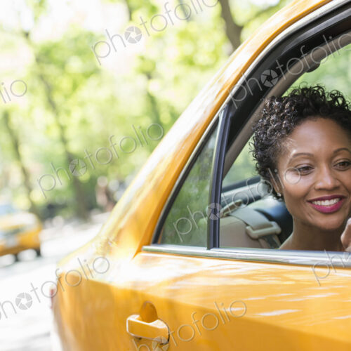 City life. People on the move. A woman sitting in the rear passenger seat of a yellow…