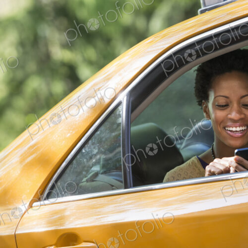 City life. People on the move. A woman sitting in the rear passenger seat of a yellow…