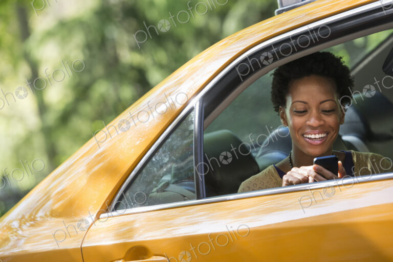 City life. People on the move. A woman sitting in the rear passenger seat of a yellow…