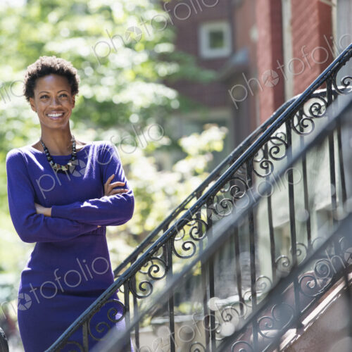 City life. People on the move. A woman wearing a purple dress, standing on the steps…