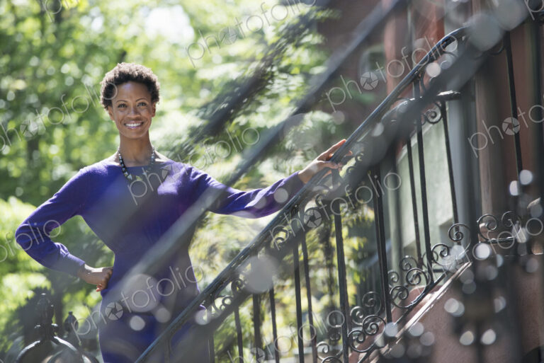 City life. People on the move. A woman wearing a purple dress, standing on the steps…