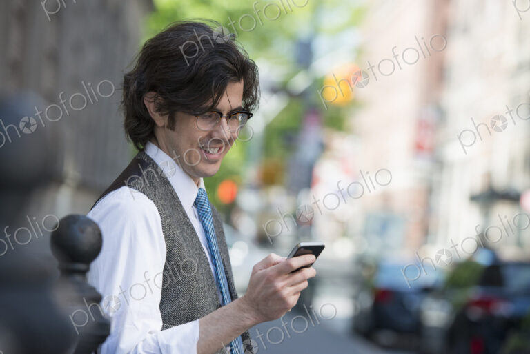 City life. People on the move. A young business man on the street checking his smart…
