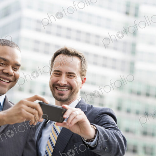 City life. People on the move. Two men in business suits, looking at a smart phone,… City life. People on the move. Two men in business suits, looking at a smart phone,…