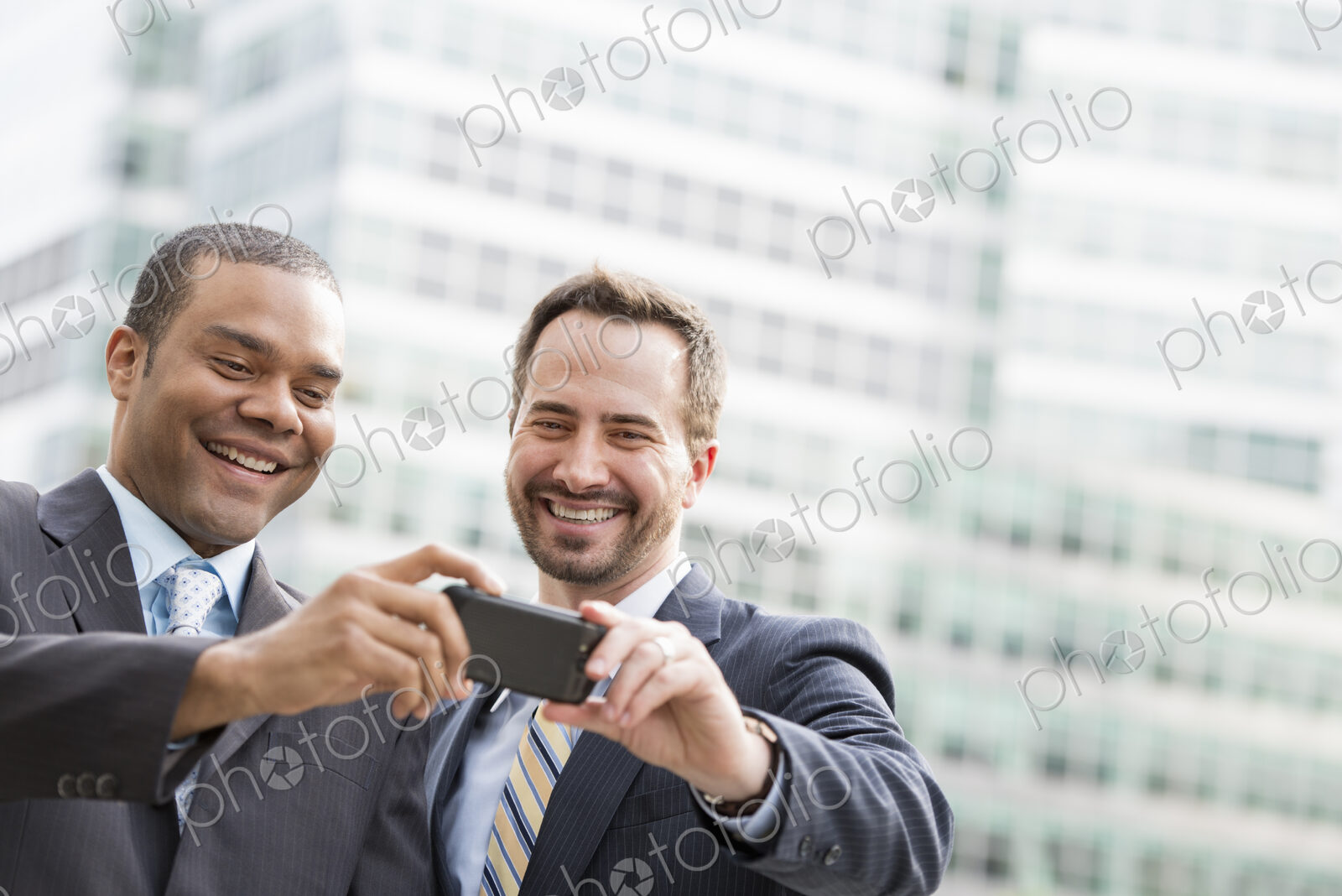 City life. People on the move. Two men in business suits, looking at a smart phone,…