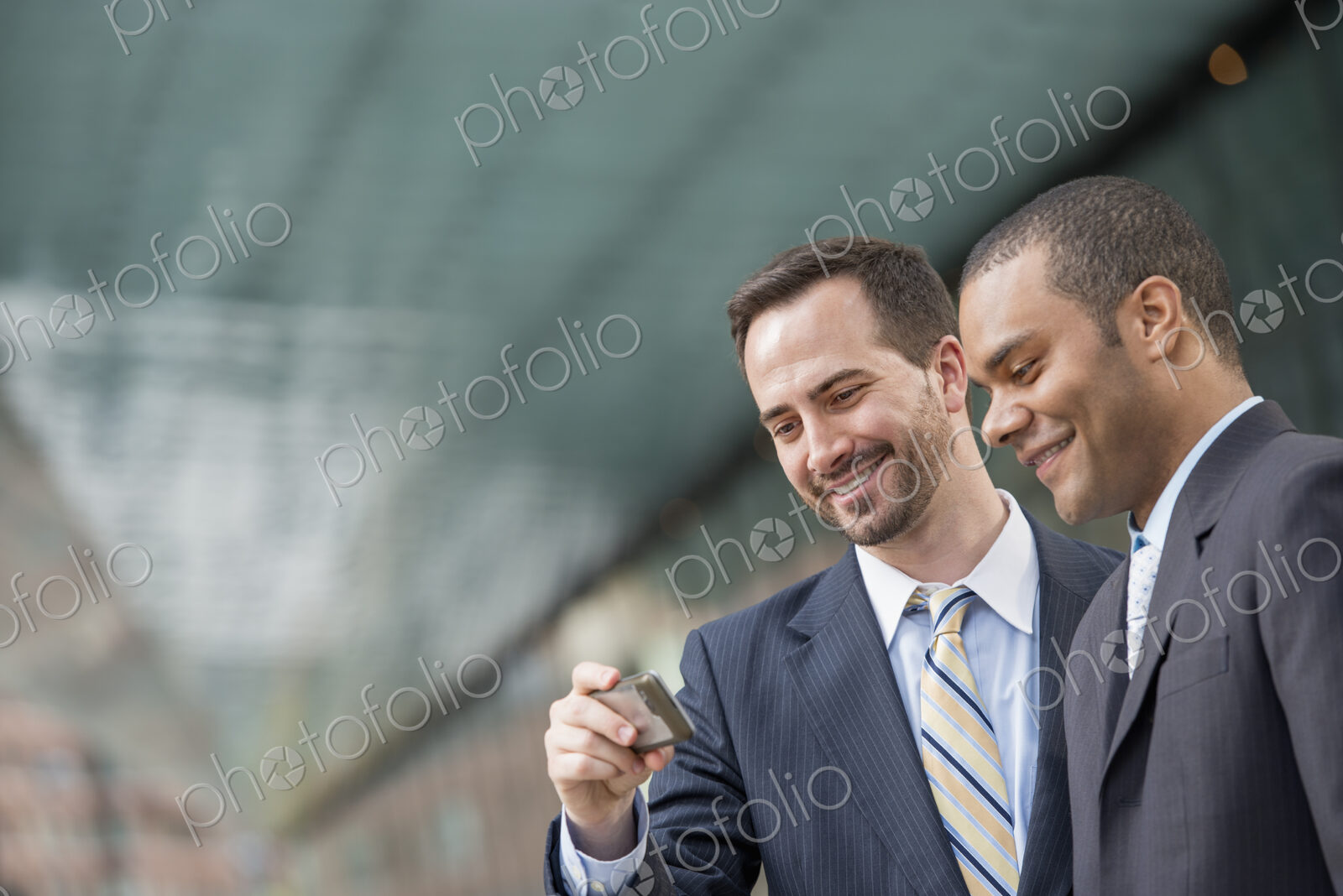 City life. People on the move. Two men in business suits, looking at a smart phone,…