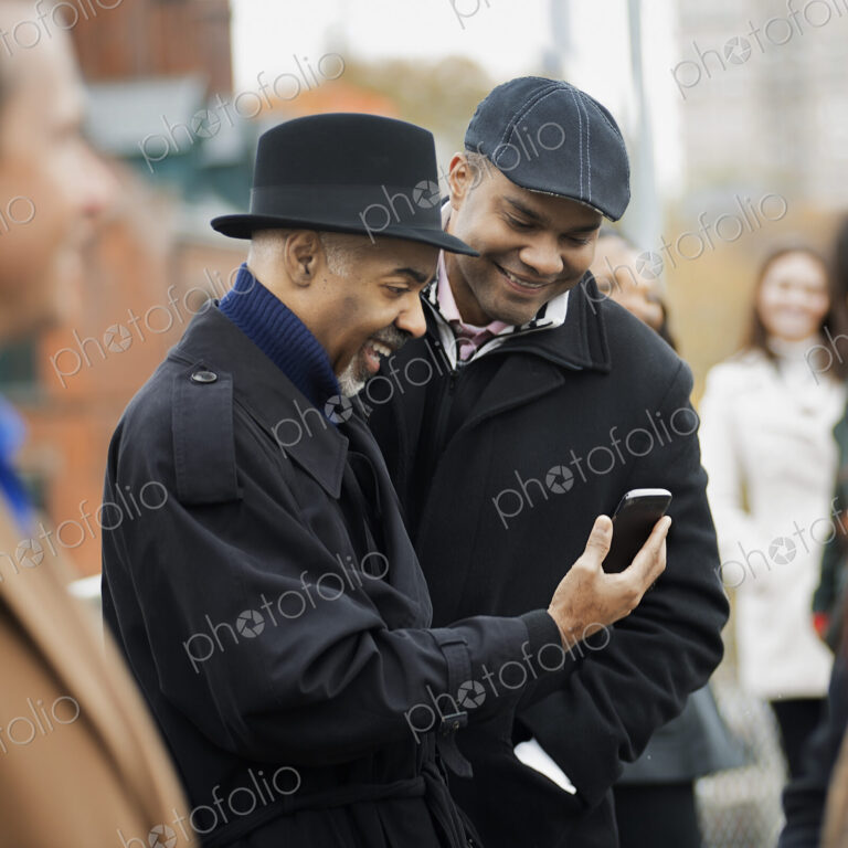 City life. Two men standing side by side, keeping in contact, using mobile phones, and…
