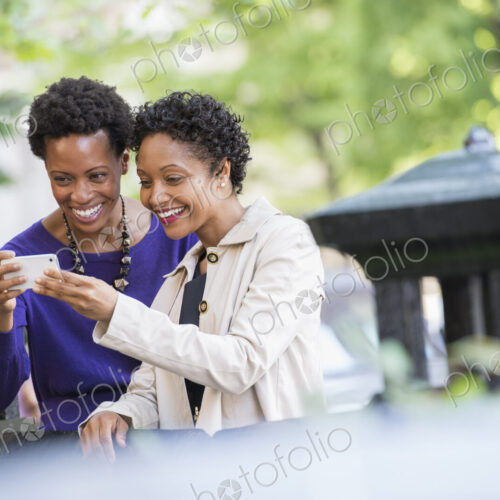 City life. Two women sitting on a park bench, looking at a smart phone. City life. Two women sitting on a park bench, looking at a smart phone.
