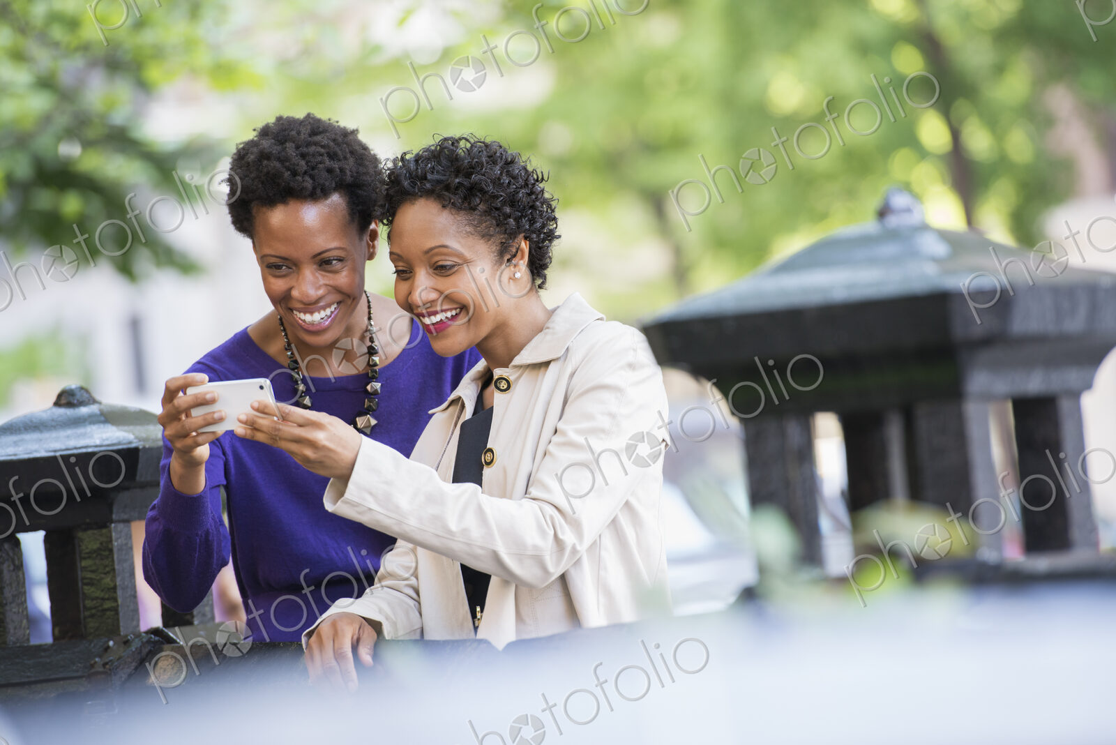 City life. Two women sitting on a park bench, looking at a smart phone.