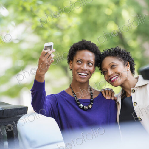 City life. Two women sitting on a park bench, side by side. Posing for a photograph… City life. Two women sitting on a park bench, side by side. Posing for a photograph…