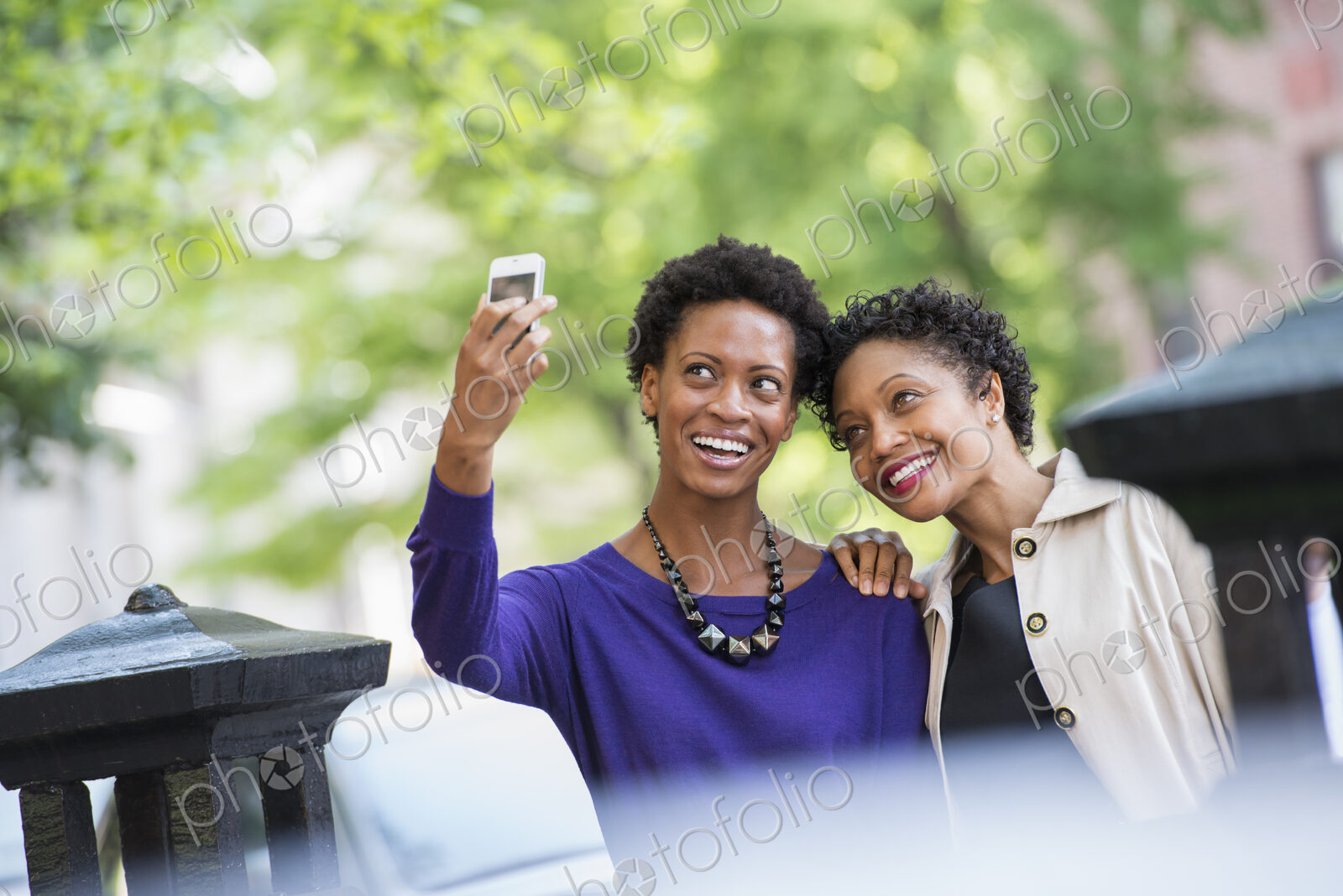 City life. Two women sitting on a park bench, side by side. Posing for a photograph…