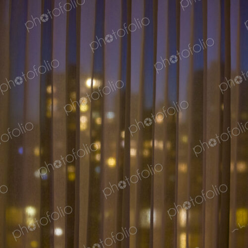City seen through blinds, buildings downtown lit up at night.