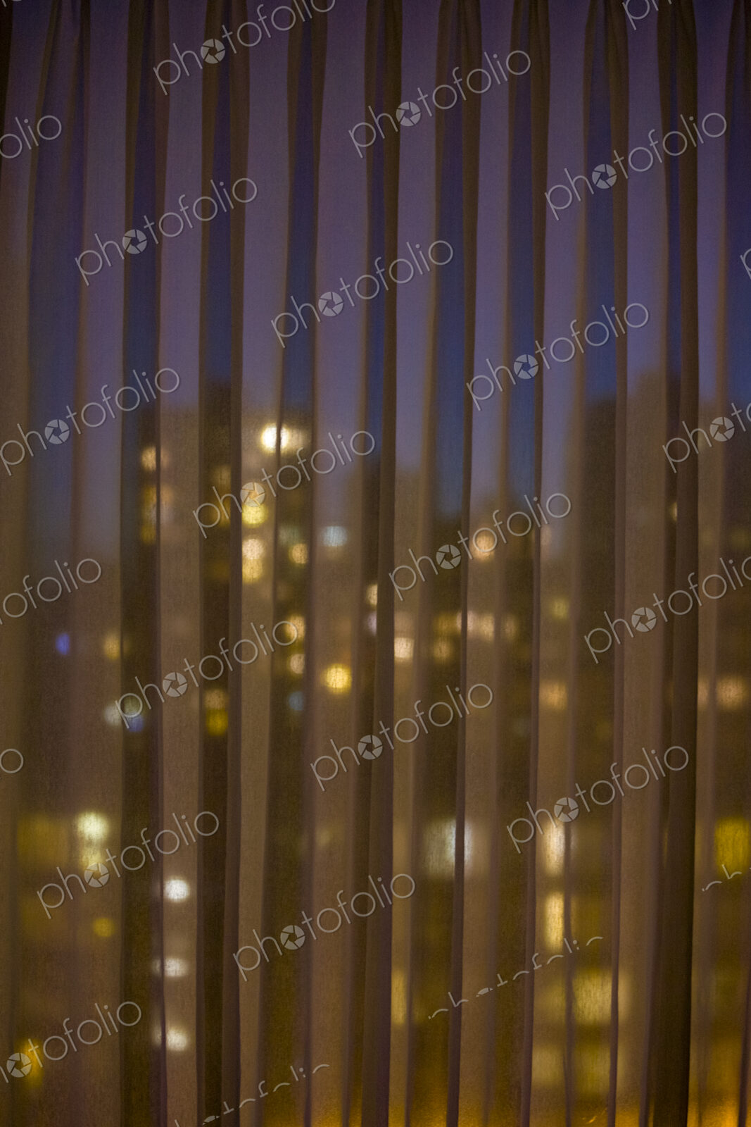 City seen through blinds, buildings downtown lit up at night.