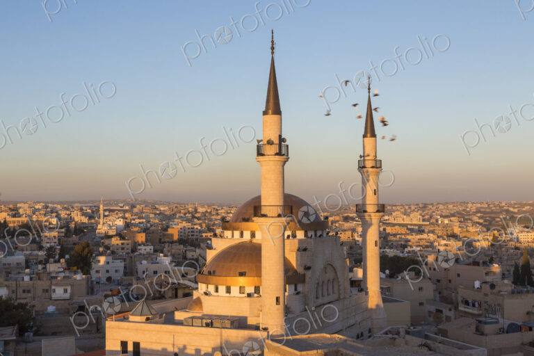 Cityscape at sunset, with mosque and minarets in the foreground.