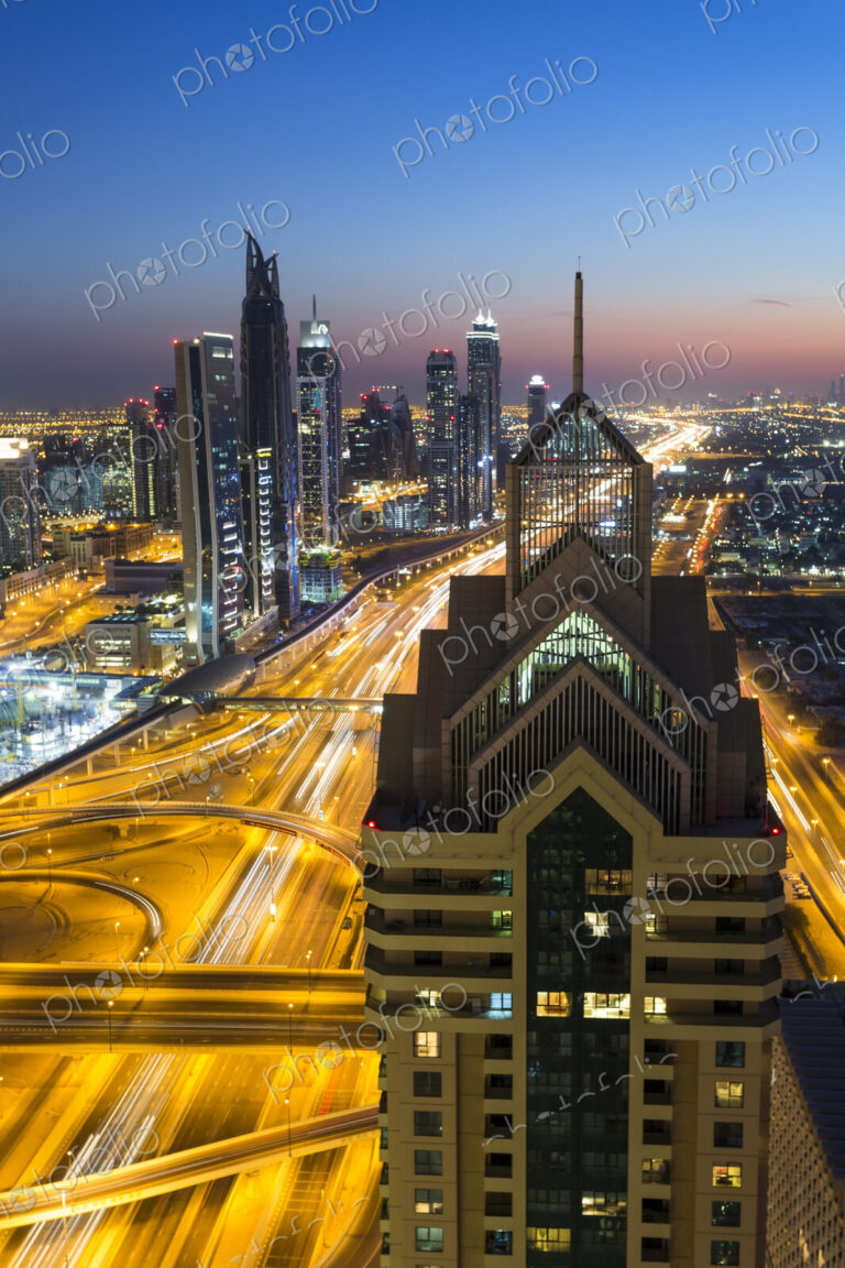 Cityscape with illuminated skyscrapers and light trails on highways at dusk.
