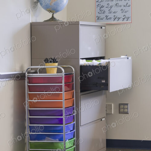 Classroom filled with equipment including filing cabinet, globe, and handwriting poster.