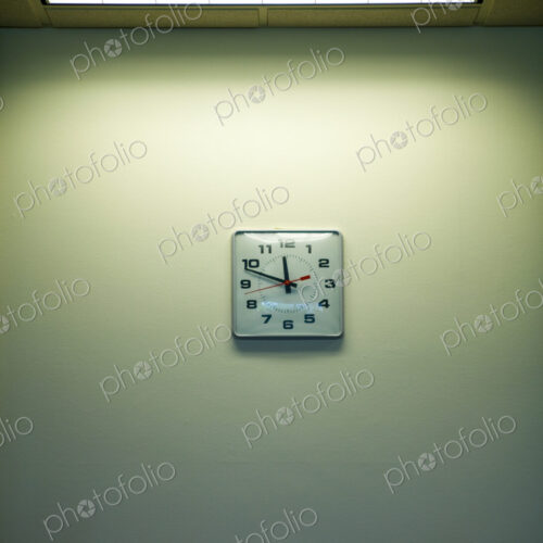 Clock on an office wall under a strip light, time nearly 11.50. Clockwatching.